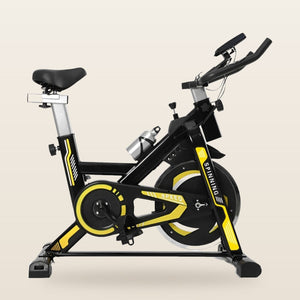Bicicleta spinning com detalhes amarelos, suporta até 150 kg, em fundo off-white